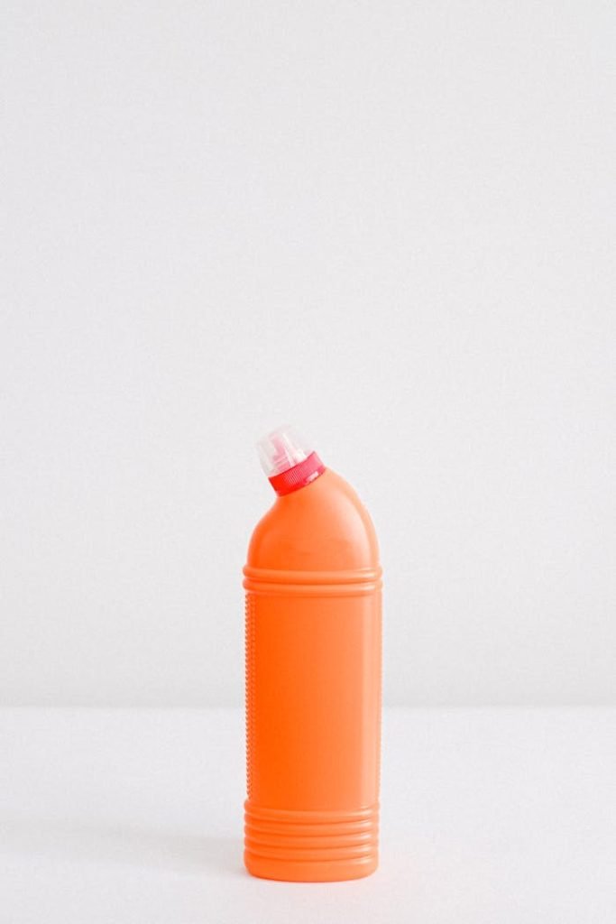 Orange plastic cleaner bottle with dispensing cap on white background.
